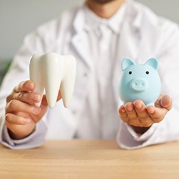 A dentist holding a large model tooth and a light blue piggy bank