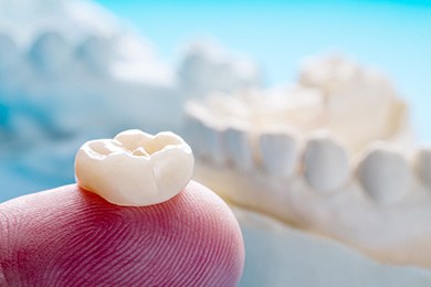 A closeup of a dental crown sitting on a person’s finger