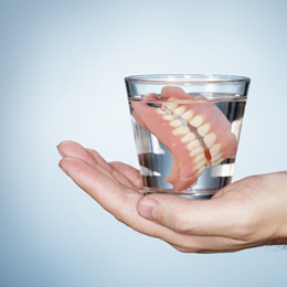 A hand holding dentures in a glass of solution