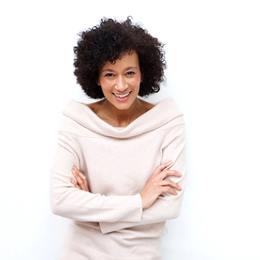 A middle-aged woman wearing a cream-colored blouse and standing with her arms folded and smiling after receiving a positive report from her dentist