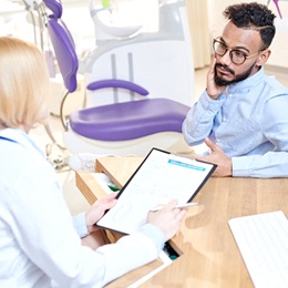 A male patient holding his cheek in pain while speaking to a female dentist about the possibility of a tooth-colored filling