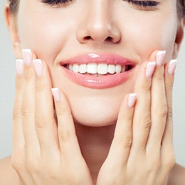 A young woman holding her face between her hands and smiling after receiving her new tooth colored filling