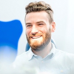 A man smiling at himself in the mirror at the dentist’s office after tooth colored filling treatment