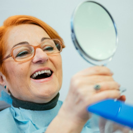 An older woman admiring her new dentures with a hand mirror