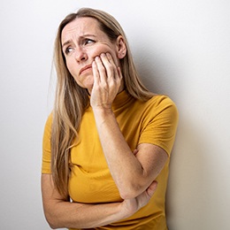 A woman wearing a yellow blouse and holding her cheek in pain in Arlington