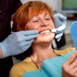 Woman in dentist's chair looking at smile after dental implant retained denture placement