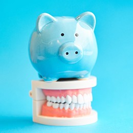 Piggy bank atop model teeth symbolizing the cost of dental implants