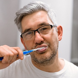 Man brushing his teeth to care for his dental implants in Arlington