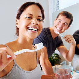 Young couple smiling while brushing their teeth
