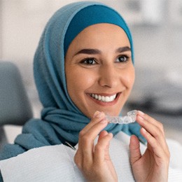 Woman smiling while holding Invisalign aligner