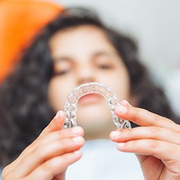 A blurred teen girl holding an Invisalign tray in front of herself
