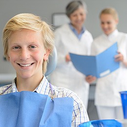 A smiling teen boy sitting in front of some blurred dentists