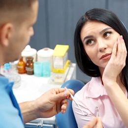 A young female holding her cheek in pain while listening to the dentist explain the need for a root canal