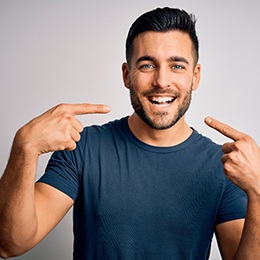 A young man wearing a blue shirt points to his smile that needs to be whitened