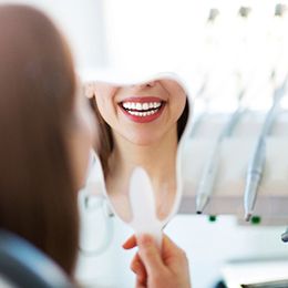 A woman looking at her whiter, brighter smile in the mirror during a regular checkup