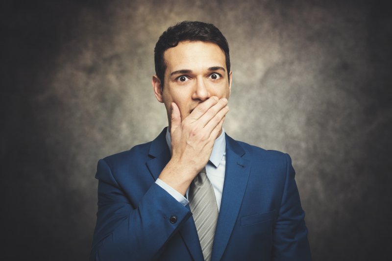 a man dressed in a suit and covering his mouth because he is embarrassed by his smile and breath