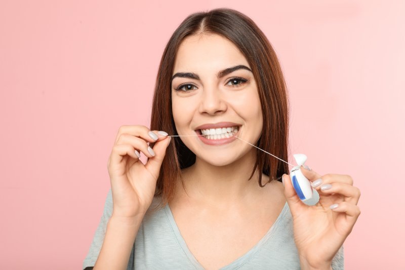 a young woman wearing a gray shirt and flossing her teeth