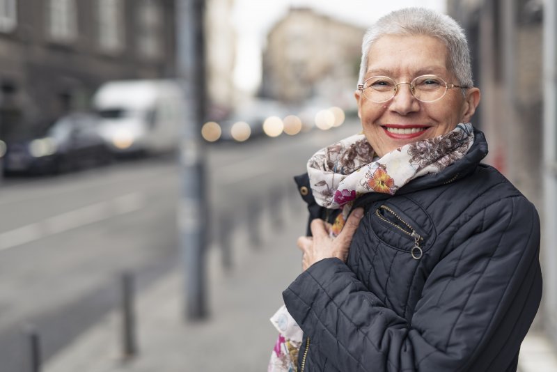 an older woman wearing a scarf and coat while standing outside and smiling