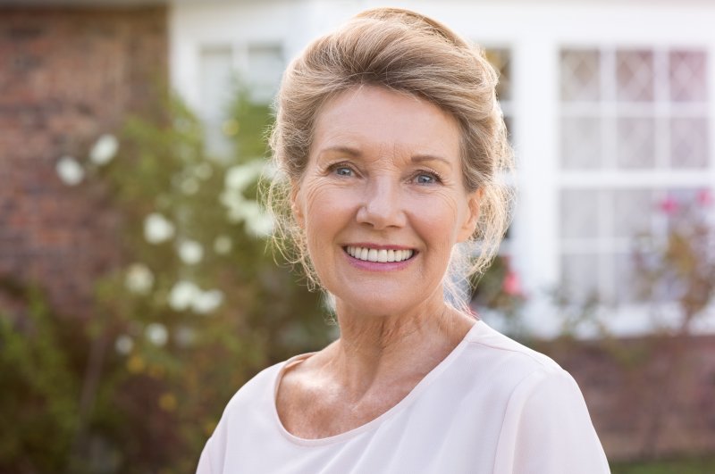 an older woman standing outside her home smiling and showing off her new dental implants