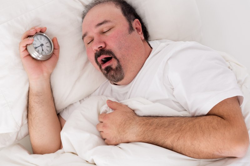 a man holding a small clock in his hand while asleep with his mouth open