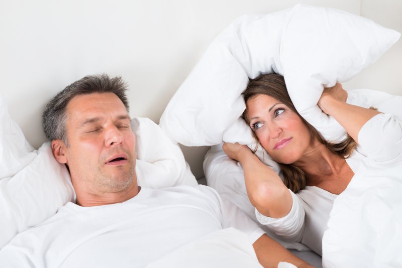 a man snoring while a woman lying next to him covers her ears with a pillow