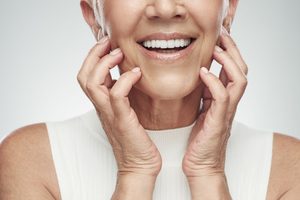 Nose-to-shoulder view of woman smiling and touching fingers to her cheeks and jaw